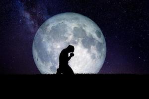 A desperate and lonely man knelt down and prayed to God. There is a moon in the background at night. Desperate, heartbreaking, and lonely concepts photo