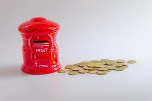 alcancía o caja de correos roja en forma de caja de dinero con pila de monedas de dinero creciendo sobre fondo blanco, enfoque selectivo foto