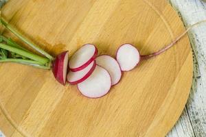 Fresh ripe radish cut into pieces on a cutting board and kitchen knife on a wooden table photo