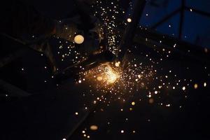 Sparks from grinding metal. Steel processing in workshop. Lights in dark. Production of parts. Cutting became grinder. photo