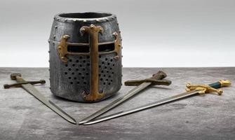 casco de caballero medieval y espadas aisladas en una mesa de piedra.