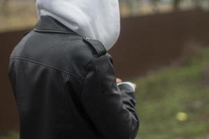 A teenager walks down the street in a gray hood and a black leather jacket, a side view. Casual clothing, autumn views. photo