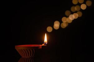 Selective focus on flame of clay diya lamp lit on dark background with bokeh lights. Diwali festival concept. photo