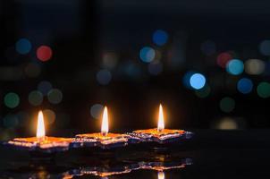 Selective focus on flame of first clay diya lamps lit on dark background with colorful bokeh lights. Diwali festival concept. photo