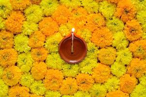 rangoli de flor de caléndula decorativa para el festival de diwali con lámpara diya de arcilla iluminada con llama de enfoque borrosa. foto