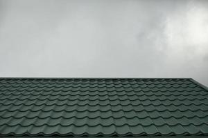 Roof of house against background of gray sky. Green roof tiles. photo