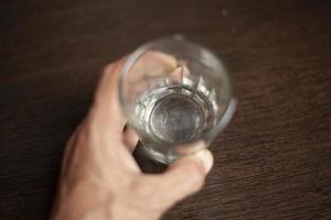 The bottom of an empty glass is in focus. Hand holds a glass mug. Capacity for liquid. photo