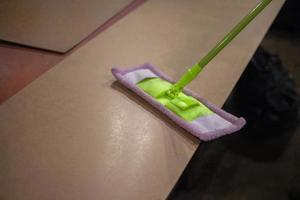 Cleaning the surface from dust with a mop. Work in the workshop requires cleanliness. Green mop with a long handle. Surface preparation for processing. photo