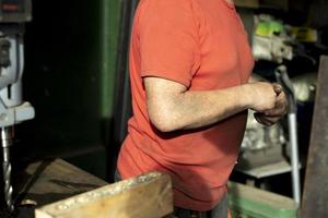 A worker in a red T-shirt behind the machine. Side view, dirty hands. Indoor work. Sunlight. photo