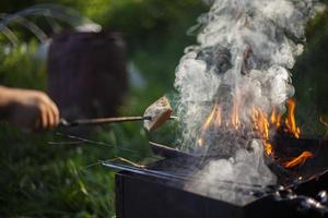 Piece of bread is baked on fire. Picnic in summer in detail. Open fire from dry branches. Cooking on flame. Rest in summer. photo