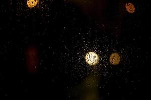 Raindrops on the glass. Blurry background with lights. The texture of the glass on a dark background. photo