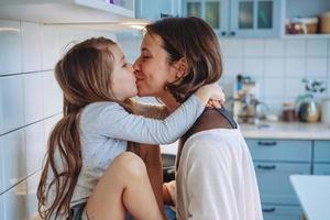 mamá besa a su pequeña hija en la cocina foto
