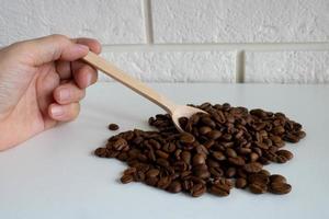 la mano sostiene una pequeña cuchara de madera con granos de café, para la producción de un delicioso café. granos de café tostados enteros para moler foto