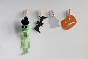 A toy skeleton in a top hat, a bat, a ghost and a pumpkin hang on clothespins. Halloween concept photo