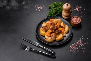 Beef meat and vegetables stew on a black plate with roasted potatoes photo