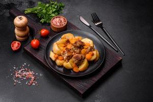 Beef meat and vegetables stew on a black plate with roasted potatoes photo