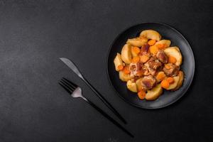 Beef meat and vegetables stew on a black plate with roasted potatoes photo