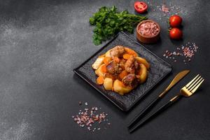 Beef meat and vegetables stew on a black plate with roasted potatoes photo