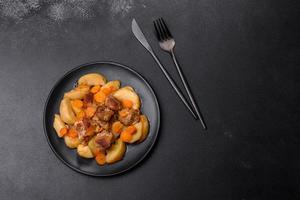 Beef meat and vegetables stew on a black plate with roasted potatoes photo