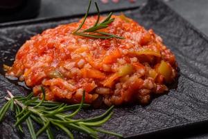 Boiled rice with peppers, spices, herbs and tomato sauce on a black slate plate photo