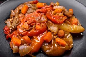 Baked vegetables, eggplant, peppers and carrots on a black plate on concrete background photo