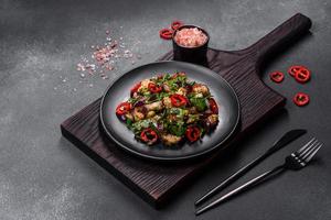 A salad of baked aubergine, sweet pepper, garlic, zucchini and parsley in a black plate photo