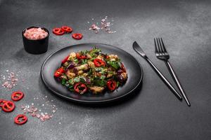 A salad of baked aubergine, sweet pepper, garlic, zucchini and parsley in a black plate photo