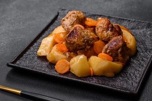 Beef meat and vegetables stew on a black plate with roasted potatoes photo