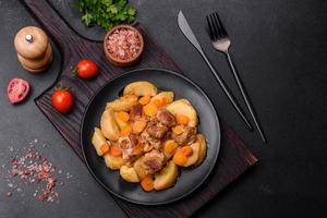 Beef meat and vegetables stew on a black plate with roasted potatoes photo