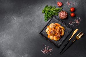 Beef meat and vegetables stew on a black plate with roasted potatoes photo