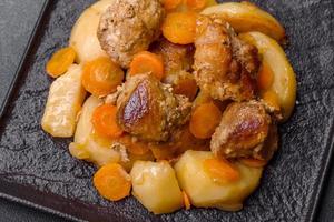 Beef meat and vegetables stew on a black plate with roasted potatoes photo