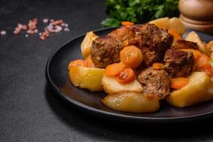 estofado de carne y verduras de ternera en un plato negro con patatas asadas foto