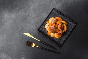 Beef meat and vegetables stew on a black plate with roasted potatoes photo