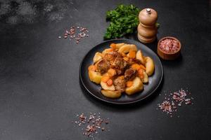 Beef meat and vegetables stew on a black plate with roasted potatoes photo