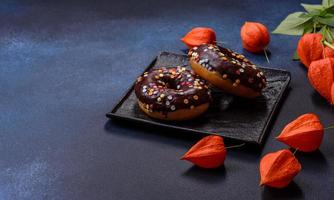 Pastries concept. Donuts with chocolate glaze with sprinkles, on a dark concrete table photo