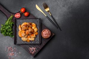 Beef meat and vegetables stew on a black plate with roasted potatoes photo