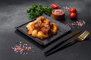Beef meat and vegetables stew on a black plate with roasted potatoes photo