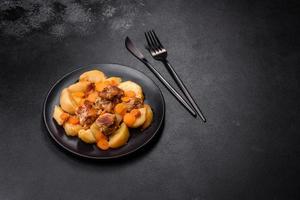 Beef meat and vegetables stew on a black plate with roasted potatoes photo