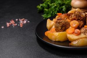 Beef meat and vegetables stew on a black plate with roasted potatoes photo