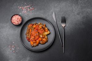 Baked vegetables, eggplant, peppers and carrots on a black plate on concrete background photo