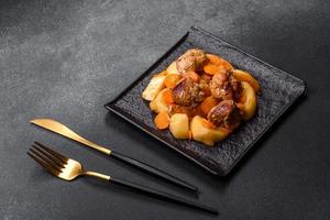 Beef meat and vegetables stew on a black plate with roasted potatoes photo