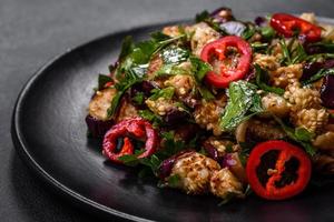 A salad of baked aubergine, sweet pepper, garlic, zucchini and parsley in a black plate photo