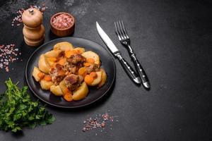 Beef meat and vegetables stew on a black plate with roasted potatoes photo