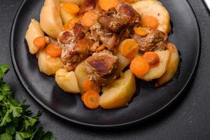 Beef meat and vegetables stew on a black plate with roasted potatoes photo