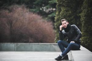 un hombre vestido con jeans y asientos de chaqueta negra en una losa foto