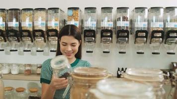 Young Caucasian female customer is choosing and shopping for organic products in refill store with reusable bag, zero-waste grocery, and plastic-free, eco environment-friendly, sustainable lifestyles. video