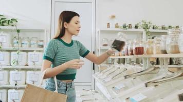 una joven cliente caucásica está eligiendo y comprando productos orgánicos en una tienda de recarga con bolsas reutilizables, comestibles sin desperdicio y estilos de vida sostenibles, ecológicos y sin plástico. video