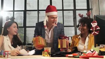 männlicher kaukasischer chef in weihnachtsmütze überrascht das weibliche mitarbeiterteam, indem er geschenke im geschäftsbüro in der weihnachtsfestparty gibt und das neue jahr vor firmenferien, genuss und glück feiert. video