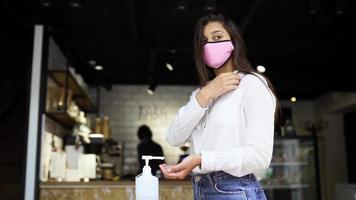 Woman wearing a pink mask disinfectiong hands with alcohol video