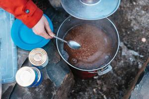Camper preparing meal in large kettle on campfire photo